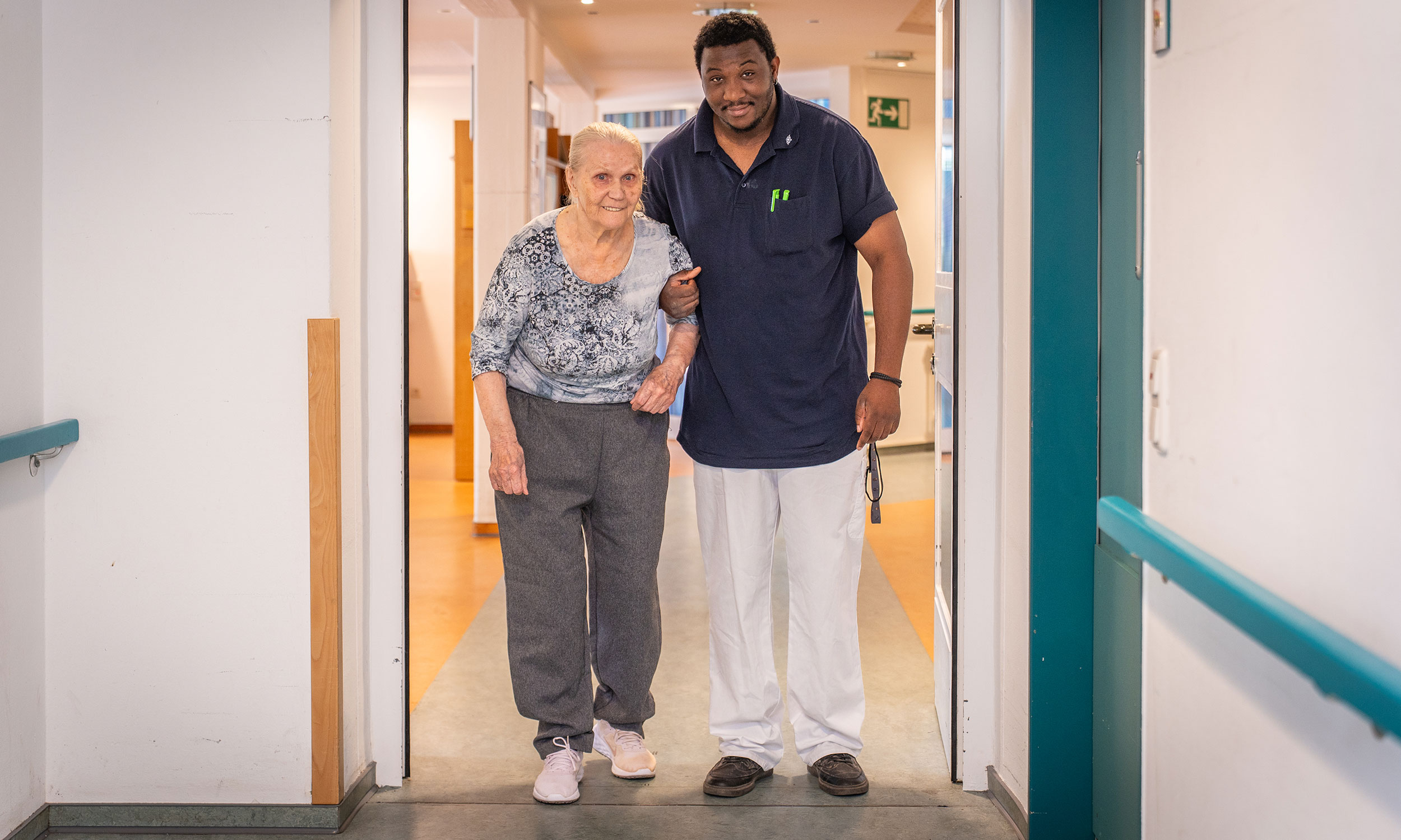 Pflegekraft und Bewohnerin stehen gemeinsam im Flur der Einrichtung